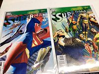 Four Superman comic books displayed in two photos, showing front covers with detailed colorful artwork typical of DC Comics series.