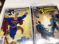 Photo of two Superman comics, Adventures of Superman #643 with Superman flying and The Last Adventures of Superman #649 showing multiple versions of Superman.