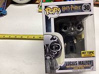 Photo shows Funko Pop figure of Lucius Malfoy in original box, measuring approx 4 to 5 inches tall, with Hot Topic exclusive sticker visible.
