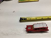 Side view of the red Husky Monkee Mobile toy car showing its approximate 3 inch length next to a tape measure.