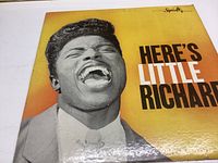 Front cover of vinyl record album 'Here's Little Richard' showing close-up image of Little Richard singing with bright yellow-orange background.