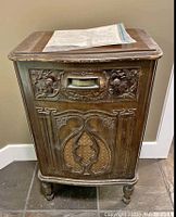 Front view of the antique wooden radio cabinet showing carved floral designs and fabric speaker grill.