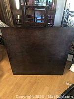 Disassembled dark wood square table top leaning against the wall showing surface condition and size.
