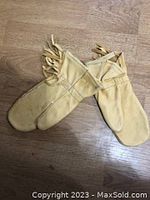 Pair of light tan vintage leather mittens with fringe detail on a wood surface, top view.
