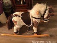 Side view of child's brown and white plush rocking horse with wooden rockers and saddle, showing battery pack location in belly.