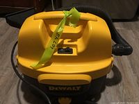 Front view of DeWalt wet/dry vacuum showing yellow top casing with handle and on/off switch, black lower body with DeWalt logo, attached power cord and flexible hose.