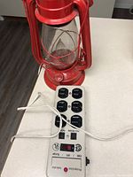 Red electric lantern sitting on a countertop with white power bar surge protector plugged in; lantern is off in this image.