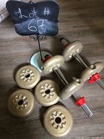 Adjustable dumbbells with vinyl-coated weight plates and red adjustment collars laid on a wood floor, along with extra weight plates.