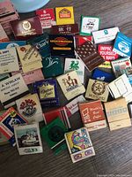 Top-down view of a spread of assorted vintage matchbooks with diverse logos and advertising designs on a wooden floor.