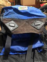Front view of MEC backpack showing blue top compartment with two black and gray diamond patches, brown fabric below, and straps.