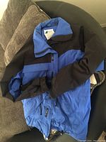 MEC ski coat folded on a chair showing blue and black color scheme and collar with tag inside.