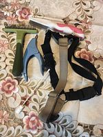 Clippers, two grooming combs, and a medium-sized pet harness laid out on a floral patterned surface.