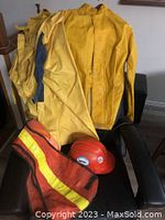 Photo showing yellow rain coat, coveralls, orange safety vest, and a yellow hard hat all laid on a chair.