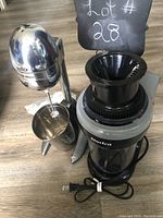 Photo showing both the Nostalgia milkshake machine with its stainless steel mixing cup and the Starfrit electric juicer with black feed chute and power cord bundled