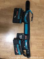 Makita tool belt laid flat showing multiple pouches and pockets designed for tool storage, made of black and teal fabric, showing signs of heavy use.