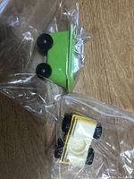 Green plastic bathtub toy with black wheels inside a clear plastic bag, viewed from the side on a wooden surface.