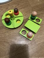 Green circular platform with 4 peg-legged plastic figures in red, brown, yellow, and green bases placed on it plus the picnic table with 2 people figures on and beside it