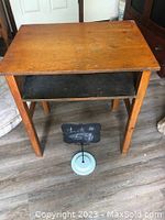 Single vintage wooden school desk with flat top and open shelf underneath, supported by four wooden legs on wood floor.