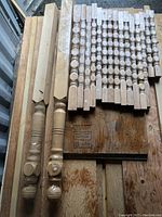 All 15 spindles laid out on wooden boards, showing turned wood detail, original shrink wrap and labels on most pieces, and exclusion of two large posts on left.