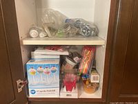 Cupboard shelf with boxed plastic cupcake stands, assorted baking cups, and small plastic accessories in packaging.