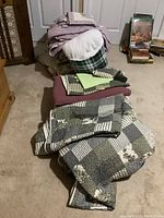 View of stacked bedding items including patchwork quilt and plaid blanket