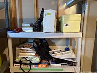 Two shelves filled with craft supplies, sewing tools, storage containers, scrapbooking materials, and binders.