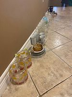 Wide view of the lot showing glass jars, ceramic mugs, amber cream servers and various glassware lined up on floor.