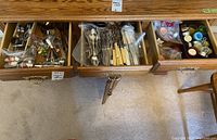 Top down view of three drawers filled with mixed flatware, serving ware, and other entertaining items in plastic bags and containers.