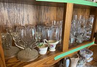Shelf with assorted glassware, cream and sugar china, and crystal stemware in wooden cabinet.