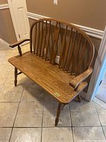 Front angled view of a wooden hall bench with spindle backrest and armrests, showing front legs and seat surface.