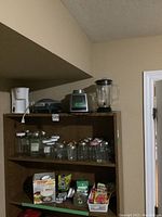 Two shelves with multiple kitchen appliances, jars and various preserving supplies including pectin, Certo, freezer jars, lids and other closures.