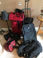 Photo of eight carry-on bags arranged together including three wheeled suitcases and five strap bags in black and red colors.