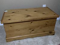 Photo of pine chest showing front and side views. Chest has a smooth natural pine wood finish with visible knots and a hinged top lid.