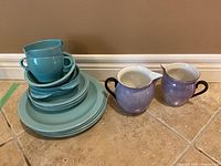 Photo showing stacked Melmac dish set including plates, bowls, and cups, and two ceramic pitchers.