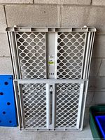 Front view of the adjustable plastic pet gate showing lattice pattern and locking mechanism.