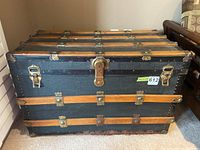 Front view of trunk showing black exterior, wooden reinforcing slats, metal locks and hardware.