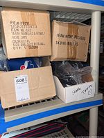Four cardboard boxes on shelf containing baseball caps. One box labeled BLUE JAYS, one labeled PACKERS. Other boxes contain caps labeled Seattle and Toronto per handwritten labels.