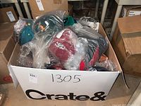Box filled with plastic-wrapped NCAA ball caps in multiple team colors and logos