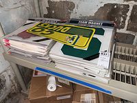 Stack of unopened NCAA team magnetic car decals, visible Oregon Ducks and large green block letter S magnet.