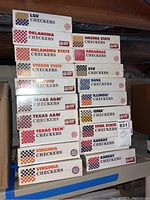 Stack of 18 boxed NCAA college football themed checkers games with various teams shown on the boxes, all sealed.