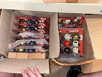 Box with multiple unopened Riddell NCAA miniature helmet sets showing varied college logos and colors.