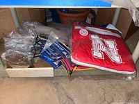Overall lot showing folded sports blankets, assorted pennants, plastic sleeves, and magnets in a box and on a concrete floor.