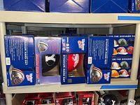 Top shelf of boxed NCAA stadium hard hats showing multiple team designs and logos on the boxes.