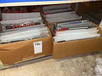 Photo of cardboard boxes filled with many stacked NFL license plate frames in original packaging, assorted teams visible along side edges.