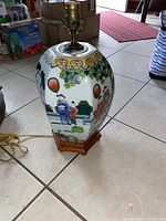 Full view of Asian porcelain table lamp base with wooden hexagonal base and brass socket fixture. Painted with traditional figures and balloon motifs. Yellow electrical cord attached.