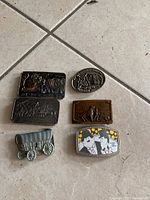 Top view of six belt buckles arranged on floor tile, showing designs and condition.