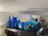 Overview of blue glassware including vases, decanters, bottles on a black metal shelf.