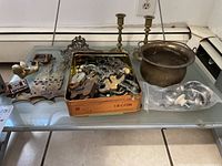 Wide view of assorted brass hardware including drawer pulls, hinges, locks, cherub figurine, brass bucket, and candlesticks arranged on glass table.