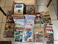 Top view of the comic book lot showing various issues including The New Titans, The Incredible Hulk, Hercules, Iron Man, Captain America, The Defenders, and more in a cardboard box and stacks.
