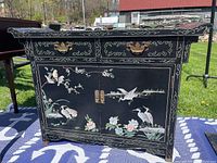 Front view of the wooden black console table with detailed Asian-style bird and floral motifs and brass handles.